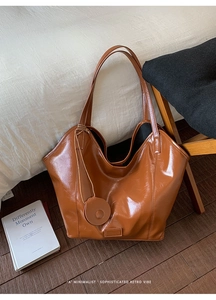 Detail view of large brown tote bag showing smooth oil wax leather texture and side charm