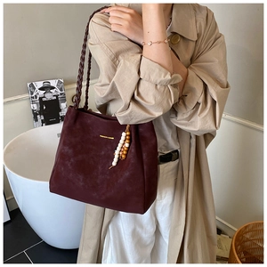 Detail of burgundy tote bag with woven straps and beaded charm on khaki trench coat