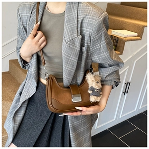 Close-up of brown leather half-moon bag with suede patchwork and cute bear charm