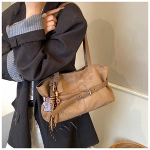 Close-up of brown suede shoulder bag with decorative belt buckle and leopard floral charm
