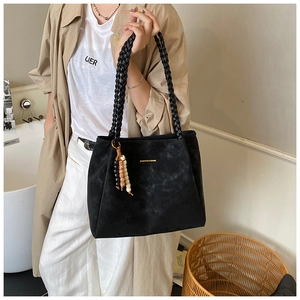 Detail of black suede tote bag featuring hand-woven handles and a beaded tassel charm