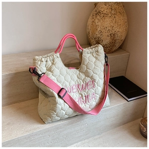Close-up of quilted beige tote bag featuring pink embroidery and adjustable strap