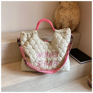 Detail of quilted tote bag featuring pink embroidered logo and contrast handles