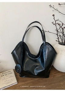 Detail of black patent leather tote bag with round charm in a minimalist studio setting