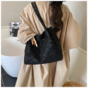 Detail of black tote bag with braided strap and wooden bead charm on a shoulder