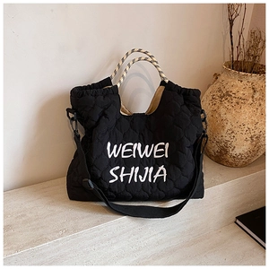 Detail of black quilted tote bag with white embroidery and woven contrast handles