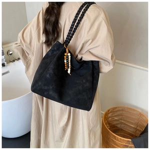 Detail of black suede tote bag with woven straps and beaded tassel charm accessory