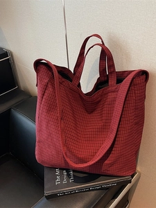 Large red checkered canvas tote bag with top handles and shoulder strap on a black sofa