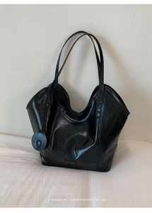 Detail of black glossy crinkled leather hobo tote bag with a small round pendant charm