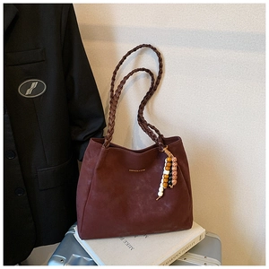 Detail of burgundy tote bag with woven handles, beaded charm and golden text