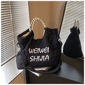 Detail of black quilted tote bag featuring white embroidery and woven top handles
