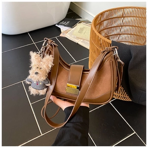 Detail of brown leather baguette bag with gold buckle and cute plush bear charm