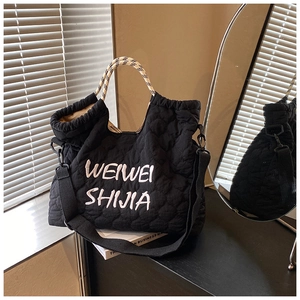 Close-up of black quilted nylon tote bag with embroidery and woven handles on a desk