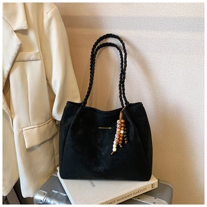 Detail of black suede tote bag with woven handles and vintage beaded charm ornament
