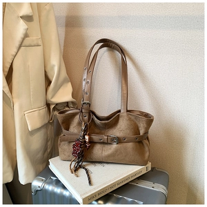 Close-up of brown suede tote bag with metal buckle belt detail and bear charm decoration