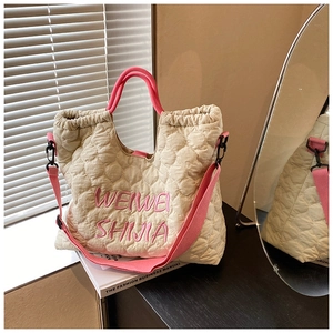 Close-up of quilted off-white tote bag with pink embroidery and contrast straps on wood surface