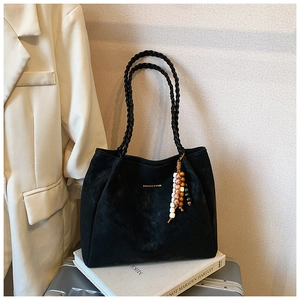 Detail view of black suede tote bag with woven handles and fashion logo in a stylish setting