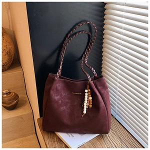 Detailed macro of burgundy suede tote bag with woven handles and beaded charm decor