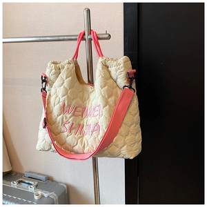 Detail of beige quilted heart tote bag with pink straps and logo embroidery