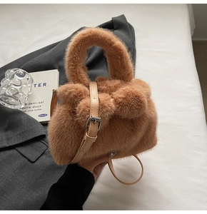 Detailed view of a brown plush bucket bag with fluffy pom-poms and leather strap