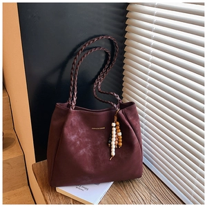 Detail of burgundy tote bag with woven handles and beaded tassel in natural lighting