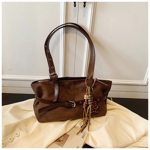 Detail of dark brown vintage suede shoulder bag with tassel charm and buckle strap