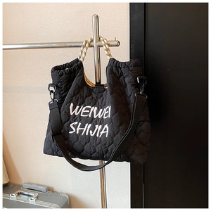 Detail view of black quilted nylon tote bag featuring white embroidered artistic lettering