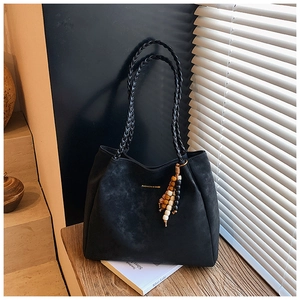 Detailed close-up of woven shoulder straps and wooden bead pendant on black suede tote bag