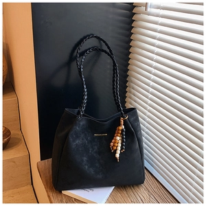 Detail of black suede tote bag with woven handles and bohemian bead charm on wooden table
