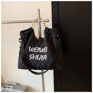 Close-up of black quilted tote bag with rope handles on display against a minimal wall