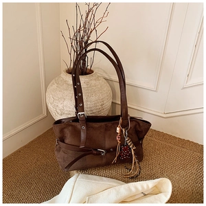 Detail of brown suede shoulder bag with decorative leather strap and ethnic heart charm