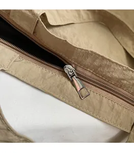 Detailed close-up of a silver polished metal zipper on khaki textured nylon tote bag