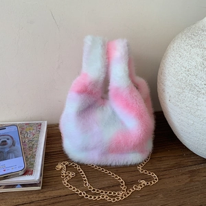 Detail of pink and white plush bucket bag with golden chain on a wooden table