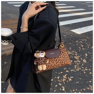 Chic leopard print shoulder bag with plush bear charm in a street style setting