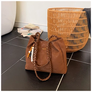 Detail of brown suede tote bag featuring woven handle and decorative beaded tassel