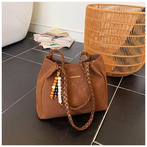 Close-up of brown suede tote bag with woven handles and decorative beaded tassel accessory