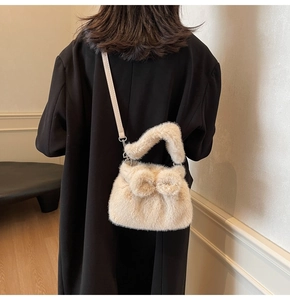 Detail of a creamy plush crossbody bag with a bow on a model wearing a black coat