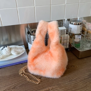 Detail of soft peach plush handbag with elegant gold metal chain strap in a lifestyle setting