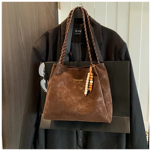 Detail of a brown suede tote bag with woven handles and a decorative beaded pendant