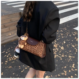 Detail of leopard print crossbody bag with brown leather flap and cute bear pendant charm