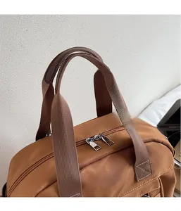 Detail of reinforced nylon handles and dual metal zippers on a brown casual shoulder bag