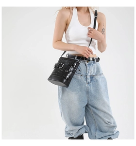 Détail d'un sac seau noir à motif crocodile avec boucle en métal et bandoulière réglable
