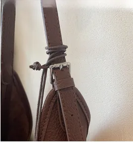 Close-up of litchi grain leather shoulder bag featuring an adjustable strap with silver buckle