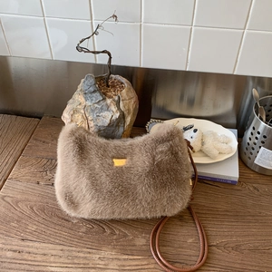 Détail du sac à bandoulière en peluche marron avec logo doré sur surface en bois