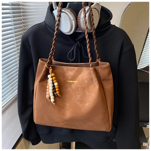 Detail of brown suede tote bag featuring braided handles and colorful beaded tassel decor