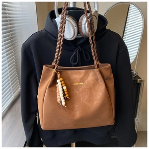 Close-up of brown tote bag with woven handles, gold lettering and beaded charm detail