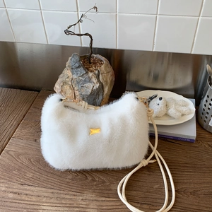 Détail d'un sac à bandoulière en peluche blanche avec plaque dorée et texture douce