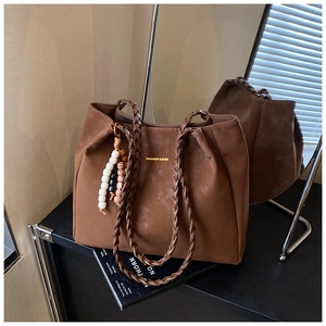 Detail of dark brown tote bag with woven handles and ethnic beaded charm accessory