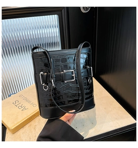 Gros plan du sac seau noir motif crocodile avec boucles métalliques et bandoulière en cuir