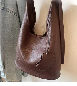 Detail of dark brown pebbled leather texture on a soft hobo bucket bag with leaf charm
